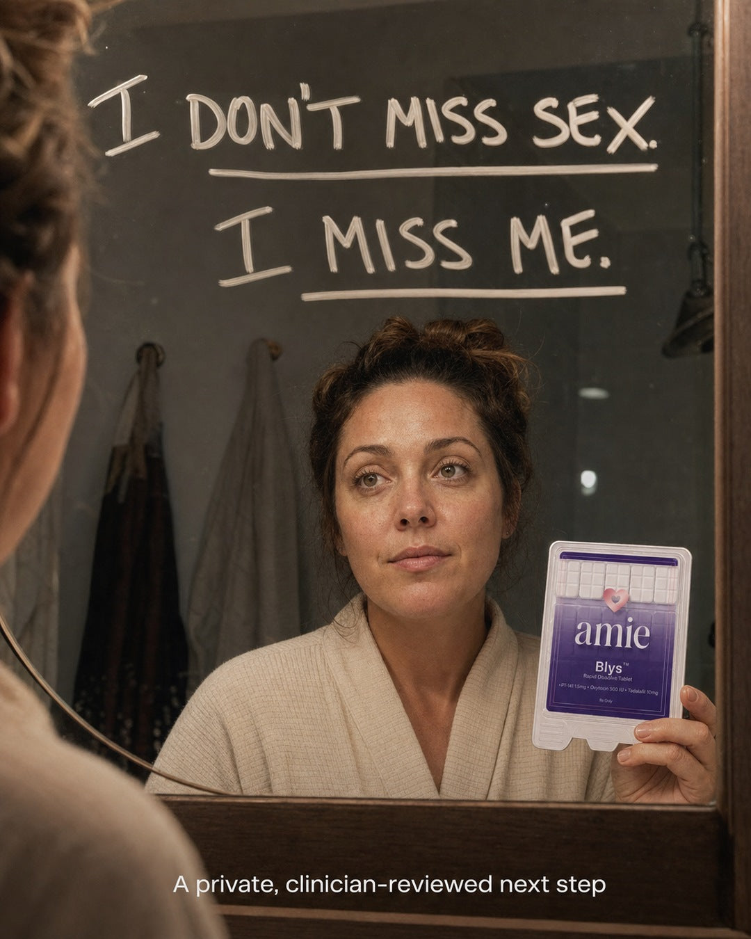 Woman looking at herself in a bathroom mirror while holding Blys by Amie