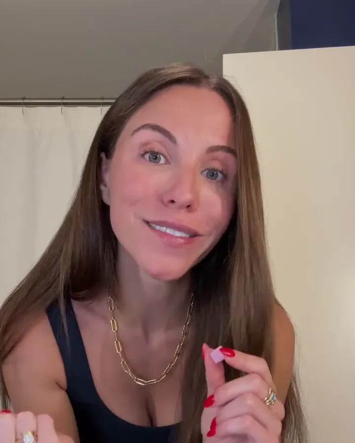 A smiling woman at home holding up a small pink tablet